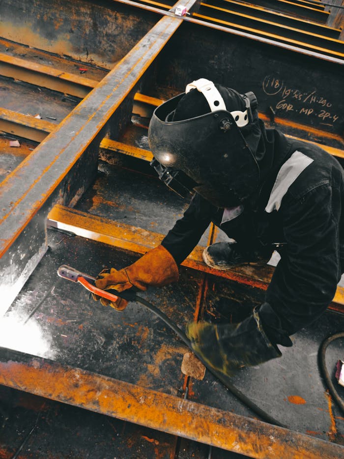 contact-img A welder in action wearing protective gear and welding helmet in an industrial setting.