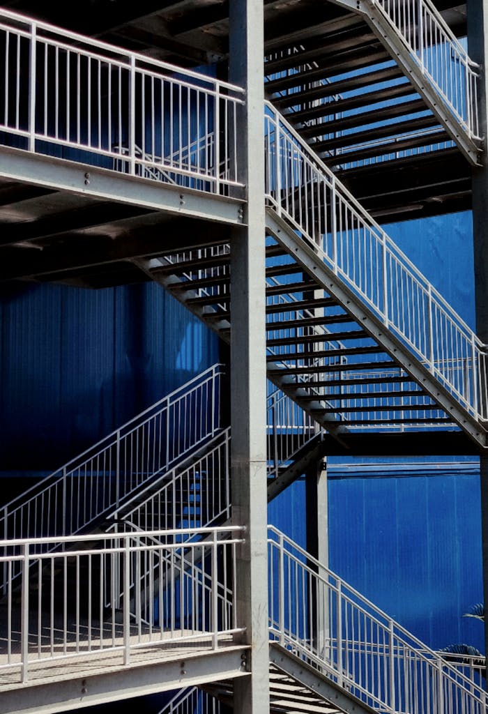 Vertical view of steel staircases against a blue building facade.