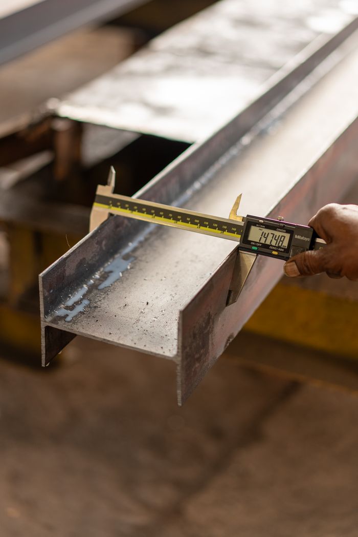 Close-up of a hand measuring a steel beam using a digital caliper in a workshop.