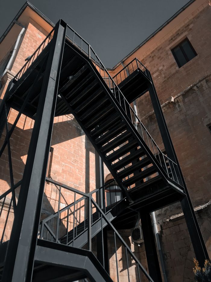 Low-angle shot of a black metal staircase attached to a brick building, showcasing industrial architecture.